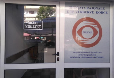 Pamje e jashtme e zyrës së Shoqatës Rajonale të të Verbërve Korçë me tabelën e orarit dhe logon
